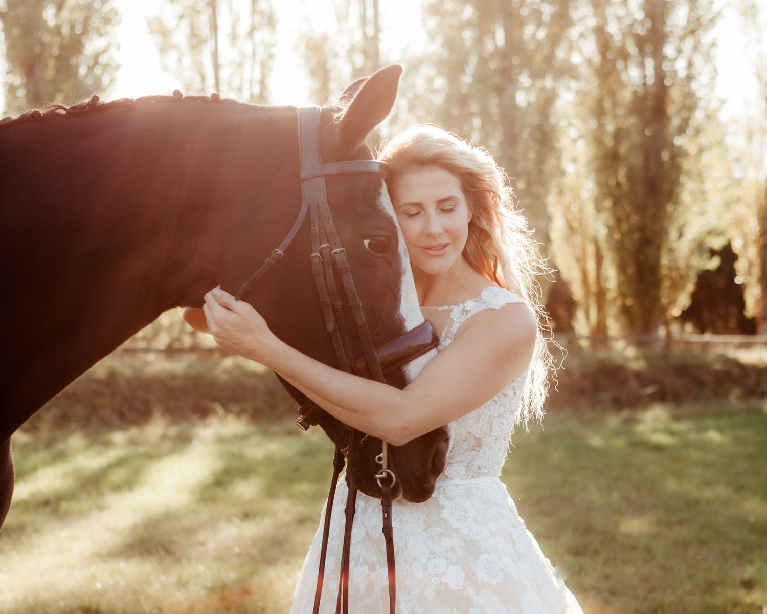 Woman in a white dress embracing a horse in a sunlit field